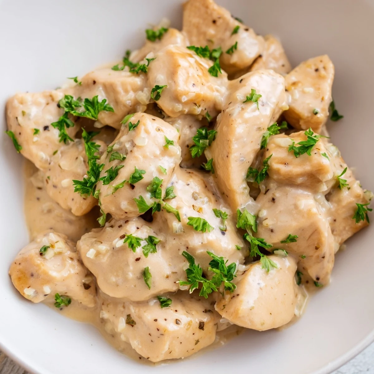 Close-up of Creamy Garlic Chicken Bites coated in a thick, cheesy garlic sauce with herbs.