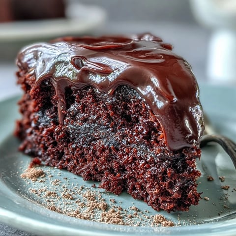 A slice of Easy Chocolate Fudge Cake reveals its moist crumb, drizzled with silky chocolate icing and served on a vintage plate.