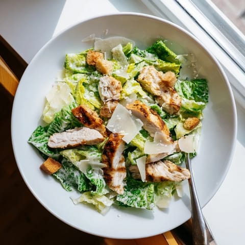 A close-up of creamy Caesar dressing drizzled over a hearty Chicken Caesar Salad, with lemon wedges and grated Parmesan nearby.