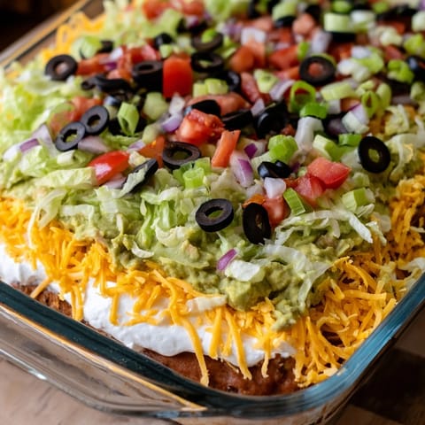 A vibrant seven-layer dip featuring seasoned beans, shredded cheese, and fresh green onions on top.