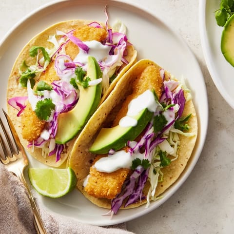 Freshly assembled Baja Fish Tacos on a plate with avocado slices, red onion, cilantro, and lime wedges for squeezing.