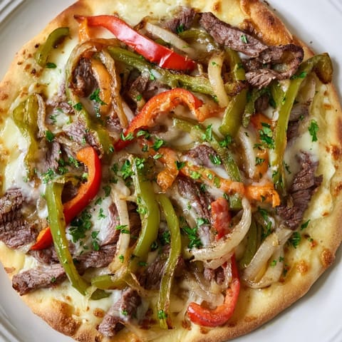 Sliced ribeye steak, sautéed peppers, and onions sit atop a crisp, golden pizza crust.