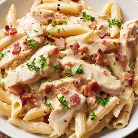 A close-up of Creamy Chicken Bacon Penne in a shallow bowl, garnished with fresh parsley and shaved Parmesan alongside a glass of white wine.
