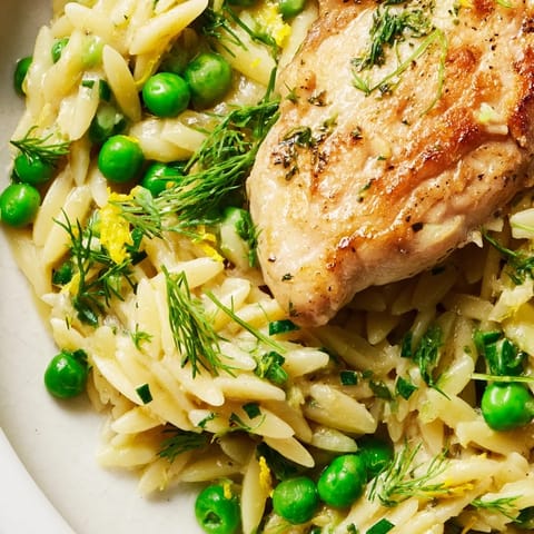 A close-up of the Lemon Herb Chicken Orzo Skillet shows juicy chicken thighs and glossy pasta coated in a fragrant lemon dill sauce.