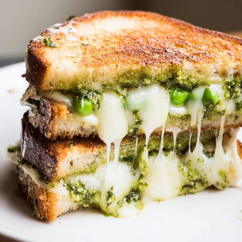Spring Pea Pesto Grilled Cheese resting on a wooden board, pesto spread visible and fresh pea garnish nearby.