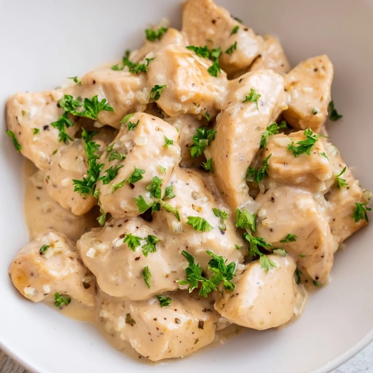 Close-up of Creamy Garlic Chicken Bites coated in a thick, cheesy garlic sauce with herbs.